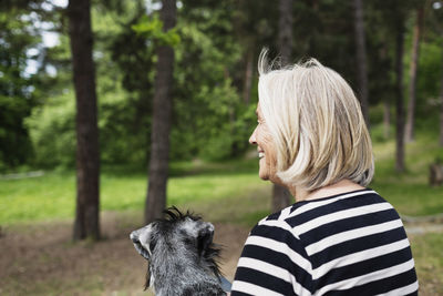Rear view of happy senior woman sitting with dog at field