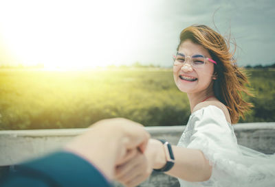 Portrait of smiling woman holding hands while standing by retaining wall