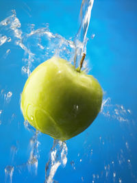Close-up of water being poured on apple against blue background