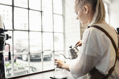 Side view of female barista preparing coffee at cafe counter by window