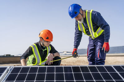 Technician measuring solar panel by colleague on sunny day