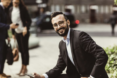 Portrait of smiling businessman with mobile phone sitting outdoors