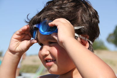 Close-up of boy wearing swimming goggles against sky