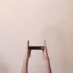 Cropped hands holding camera against wall