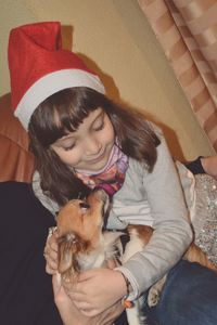 Cute girl wearing santa hat sitting with dog at home