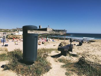 Garbage bin by people enjoying at beach against clear sky
