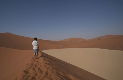 Rear view of woman walking on sand dune in desert against clear sky