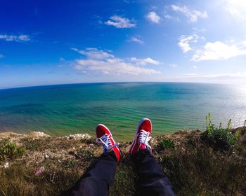 Low section of man standing by sea against blue sky