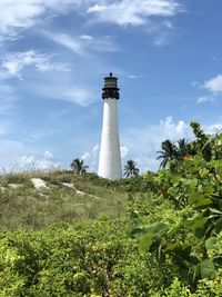 Lighthouse on field by building against sky