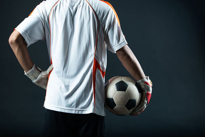 Low section of man playing soccer ball against black background