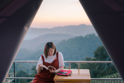 Solo asian woman traveler relax and read book with mountain background