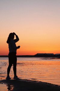 Silhouette woman standing by sea against sky during sunset