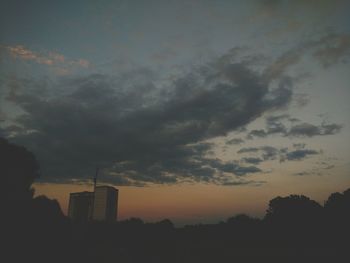 Silhouette of factory against cloudy sky