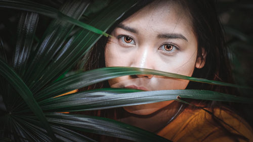 Close-up portrait of young woman wearing lens seen through leaves