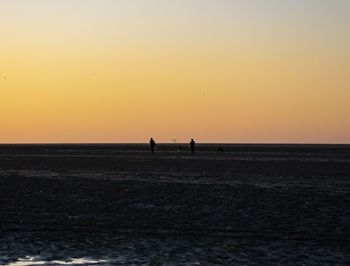 Silhouette people on beach against clear sky during sunset