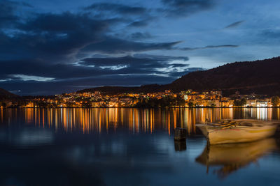 Scenic view of lake by illuminated buildings against sky