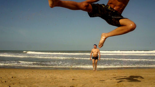 Son jumping while father walking at beach against clear sky