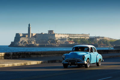 Car on road by sea against clear blue sky