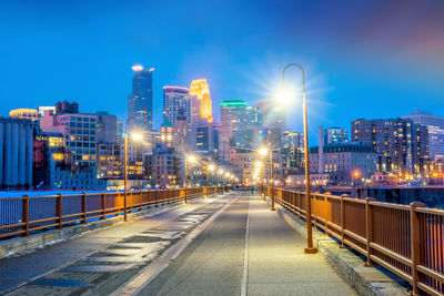 Illuminated street amidst buildings against blue sky at night