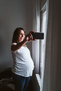 Pregnant woman taking selfie while standing at home