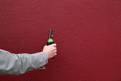 Close-up of man holding bottle against red wall