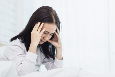 Tired woman suffering headache on bed at home