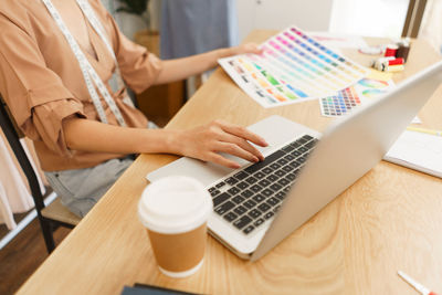 Fashion design concept, asian female designer choose color on color sample and type data on laptop.