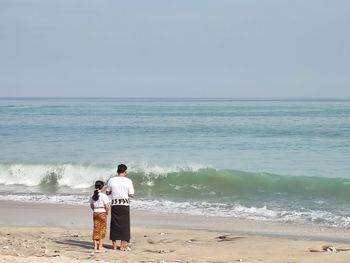 Rear view of men on beach against sky