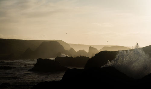Silhouette rocks by sea against sky during sunset