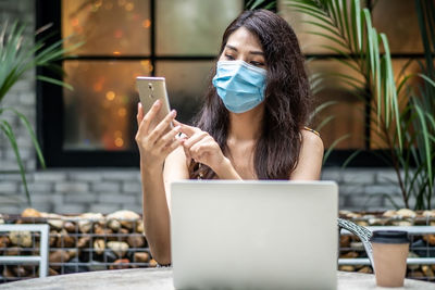 Young woman wearing mask while using phone at cafe