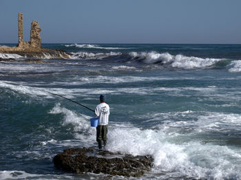 Rear view of man standing at sea shore against sky