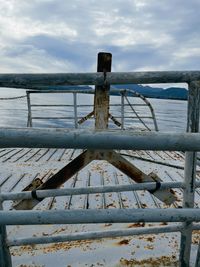 Wooden railing by sea against sky