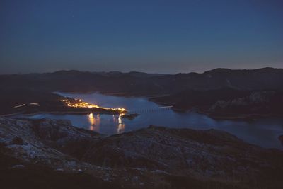 Illuminated mountain by sea against clear sky at dusk