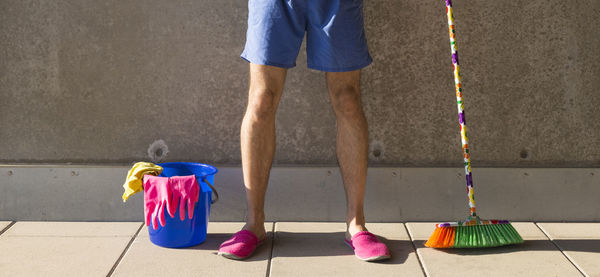 Low section of man with cleaning equipment standing against wall