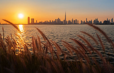 Scenic view of sea by buildings against sky during sunset