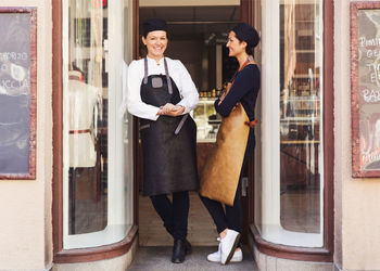 Portrait of happy female owner standing with colleague at grocery store entrance