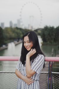 Portrait of smiling young woman standing over river on bridge