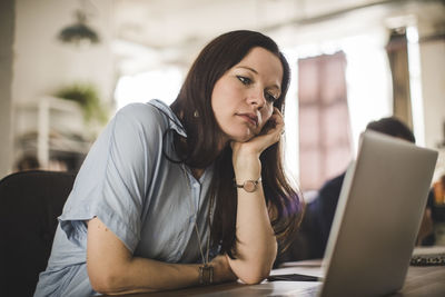 Tensed businesswoman looking at laptop while sitting at desk in creative office