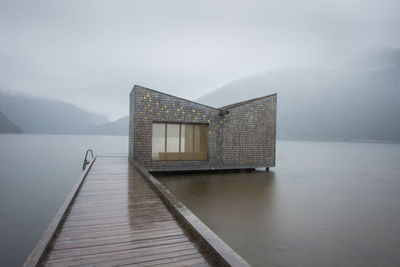 Pier to sauna by lake against sky