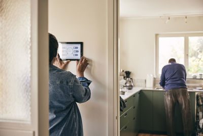 Rear view of woman using digital tablet mounted on wall at home