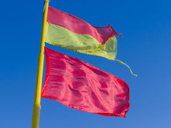 Low angle view of red flag against blue sky