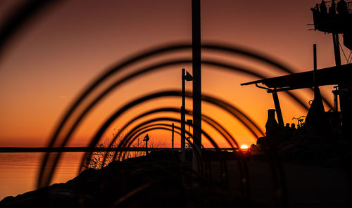 Silhouette metal by sea against sky during sunset