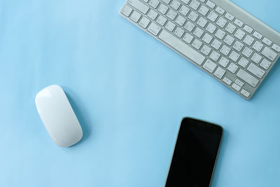 Directly above shot of computer keyboard with mouse and smart phone on blue background