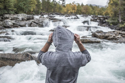 Rear view of man wearing hooded shirt by river