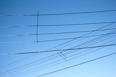 Low angle view of power lines against clear blue sky