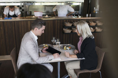 Businessman showing digital tablet to female colleague while sitting at table during meeting in restaurant