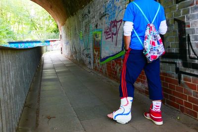 Rear view of man standing on footpath against graffiti wall