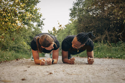 Young man practicing plank position with woman on footpath