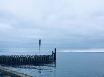 Wooden posts on pier over sea against sky