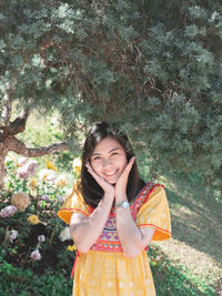 Portrait of smiling young woman standing against trees